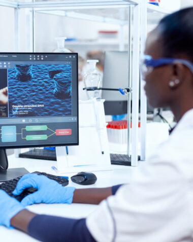 Back view of african researcher working on computer in modern faciliy. Multiethnic healthcare scientist in biochemistry laboratory wearing sterile equipment.